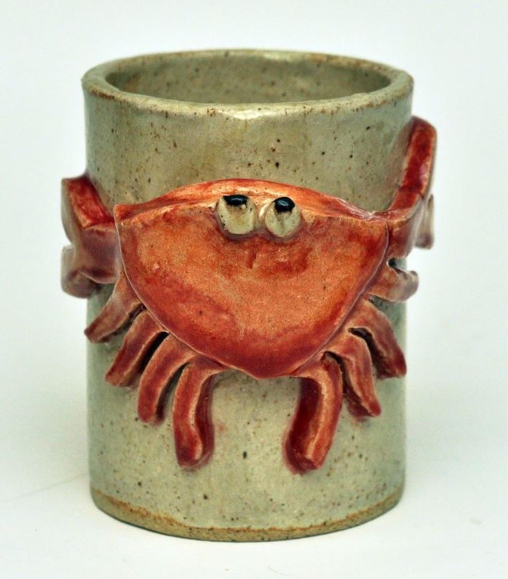 a ceramic cup with an orange crab on it's face and two black eyes