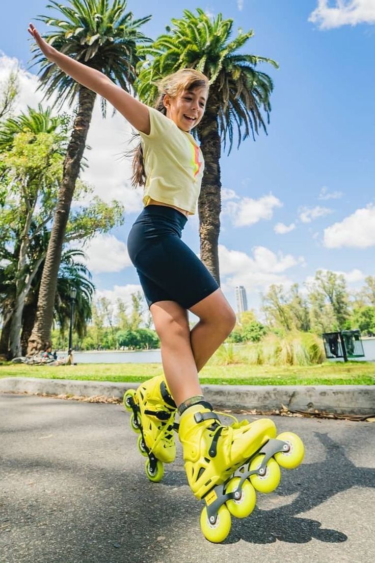 a woman in yellow shirt and black shorts doing tricks on skateboard with palm trees behind her