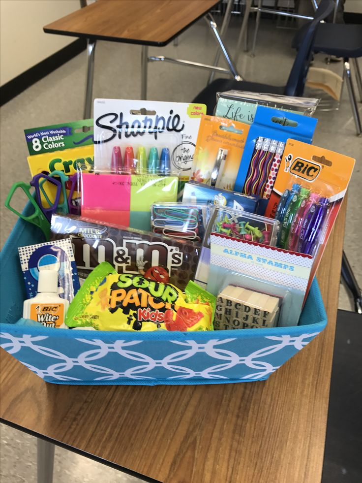 a blue basket filled with school supplies on top of a wooden table in a classroom