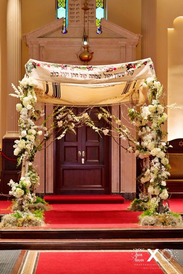 an archway decorated with white flowers and greenery in front of a red carpeted floor