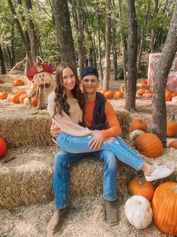 two people sitting on hay bales with pumpkins in the background