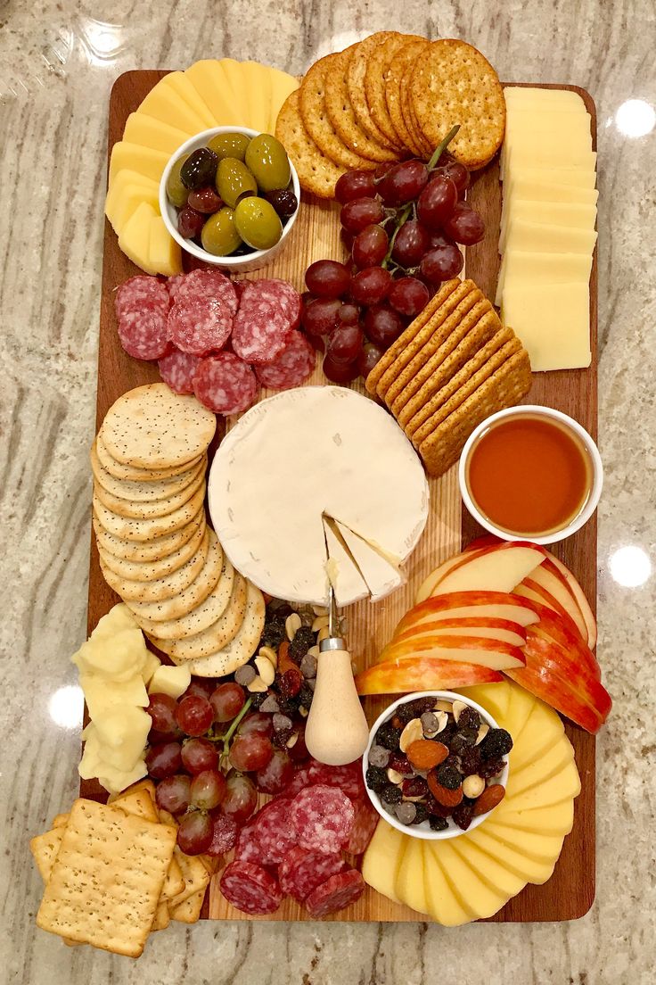 an assortment of cheeses, crackers, and fruit on a wooden platter