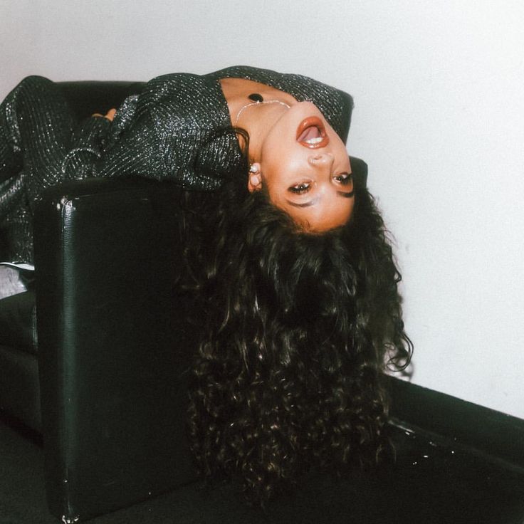 a woman laying on top of a black couch next to a wall and wearing a hat