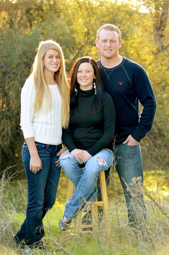 three people are posing for a photo in the grass with one person sitting on a stool