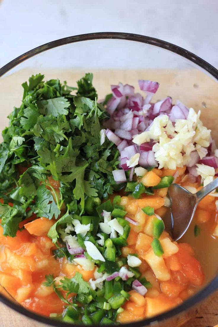 a bowl filled with chopped vegetables and cilantro on top of a wooden cutting board