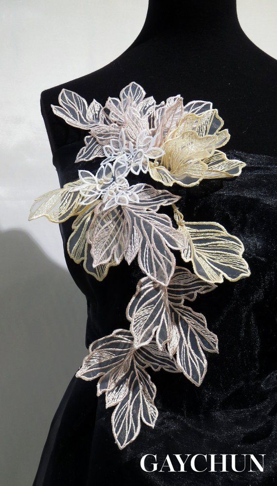 a black dress with white flowers on it and gold leaves attached to the waistline