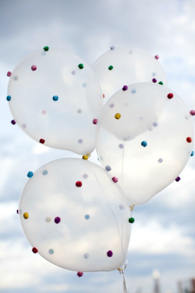 three white balloons with multicolored confetti on them in the air against a cloudy sky