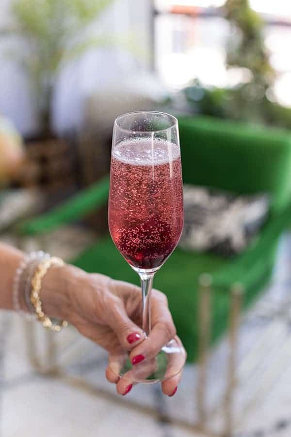 a woman holding a wine glass filled with pink liquid on top of a white table