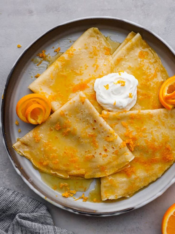 a plate with oranges and crepes on it next to some whipped cream