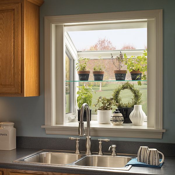 a kitchen sink sitting under a window with potted plants on the windowsill in front of it