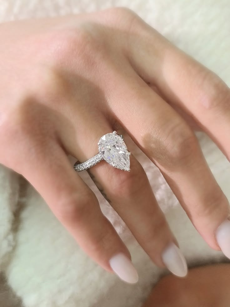 a woman's hand with a diamond ring on her finger and white manicured nails