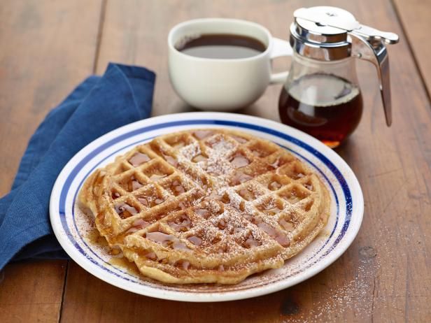 a plate with some waffles on it next to a cup of coffee and syrup