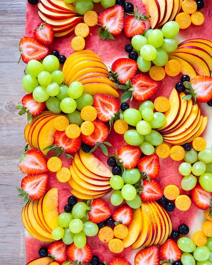 an arrangement of fruit arranged on top of a watermelon and grape tray with blackberries, oranges, grapes, and strawberries