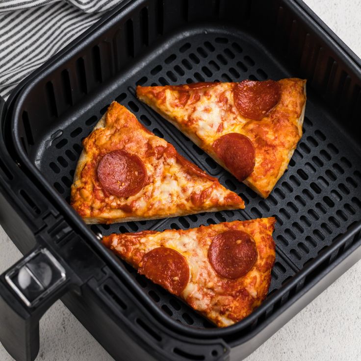 three slices of pepperoni pizza sitting on top of an air fryer pan,