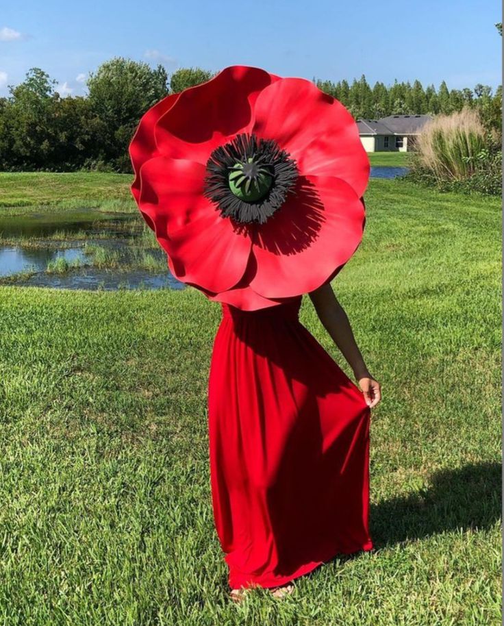 a woman in a long red dress holding a large flower on top of her head