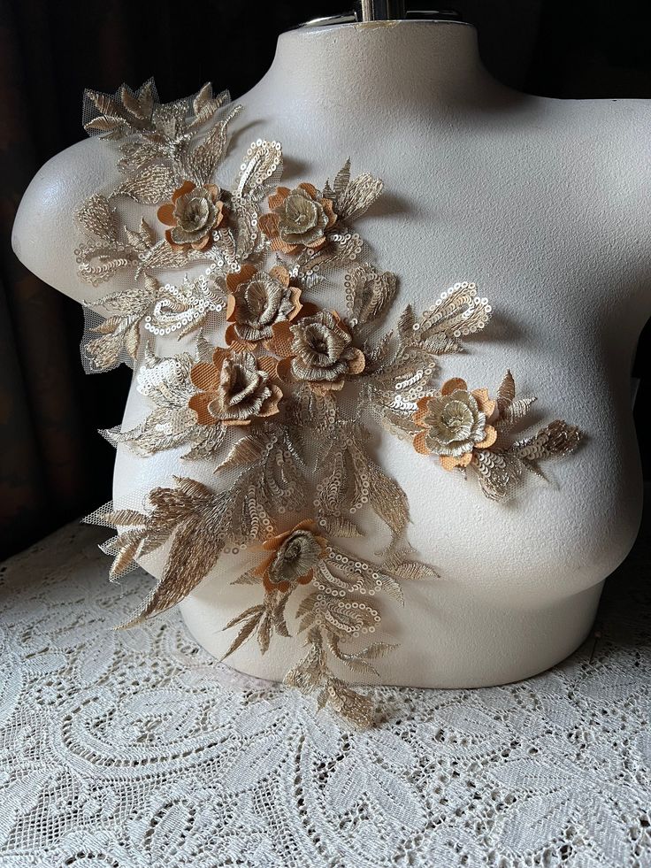 a white mannequin with flowers on it's back and gold leaves around the neck