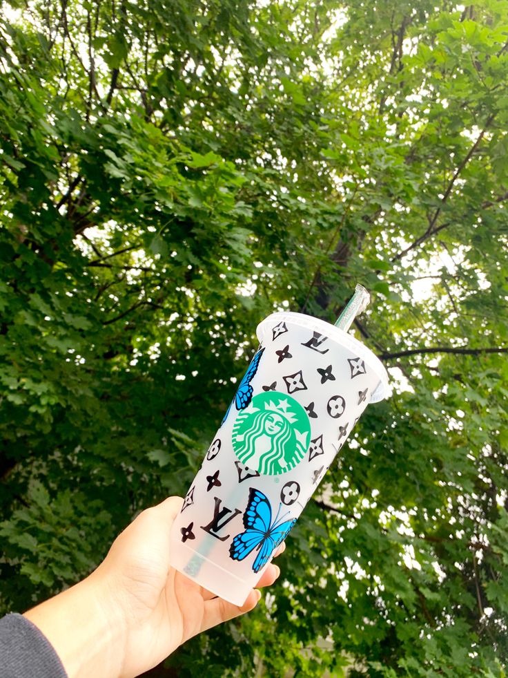 someone holding up a starbucks cup in front of some trees