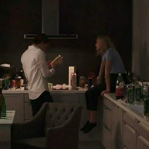 a man and woman standing in a kitchen next to a counter with bottles on it