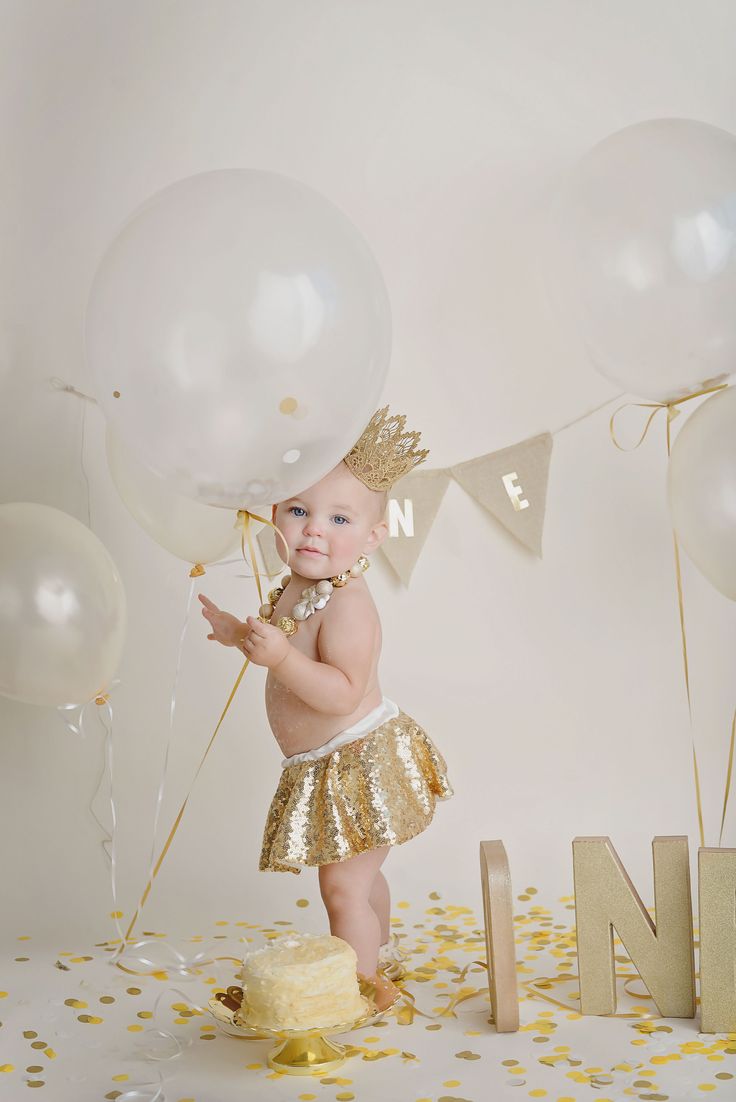 a baby girl standing on top of a cake surrounded by balloons