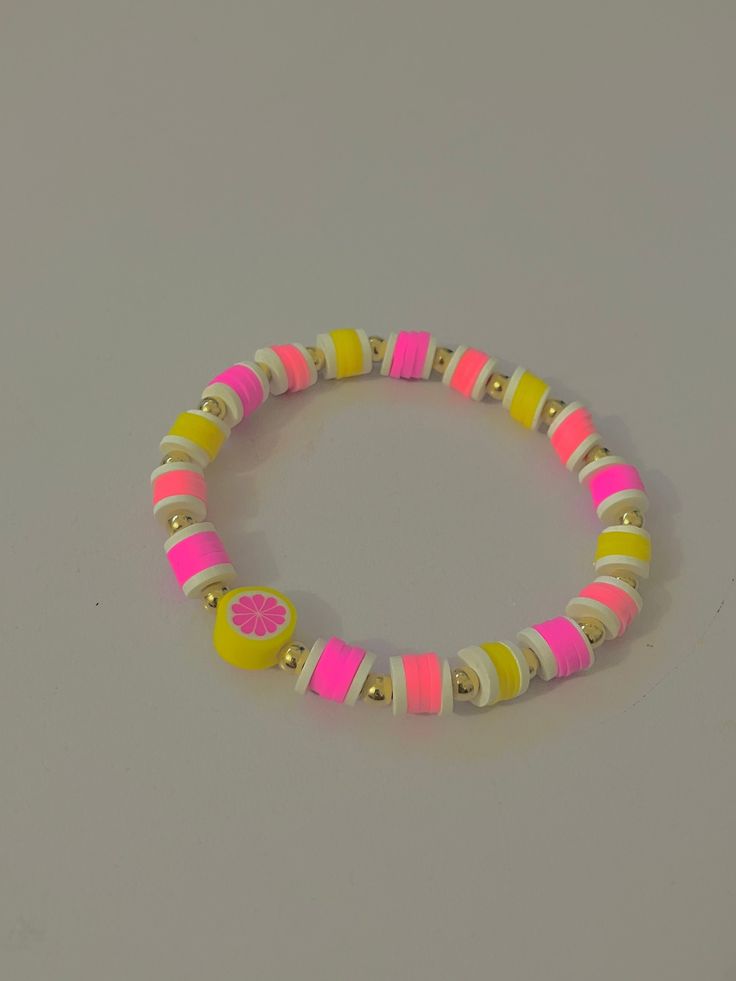 a pink, yellow and white beaded bracelet on a gray surface with gold accents