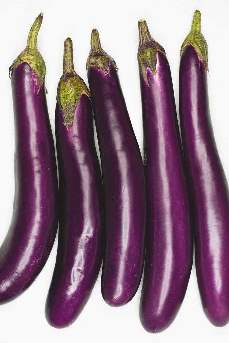 five purple eggplant's are lined up on a white surface