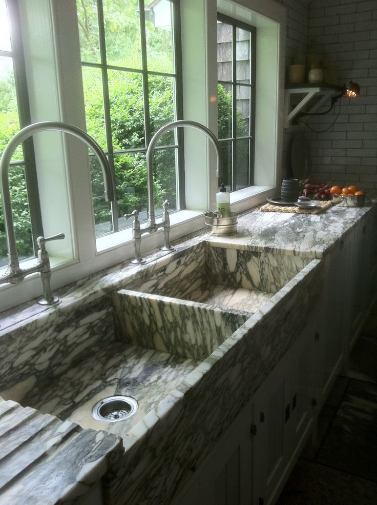 a kitchen with marble counter tops and double sinks in front of large windows overlooking trees