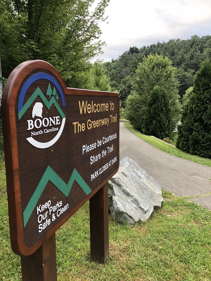 a sign that is in the grass near some rocks and trees with a sky background