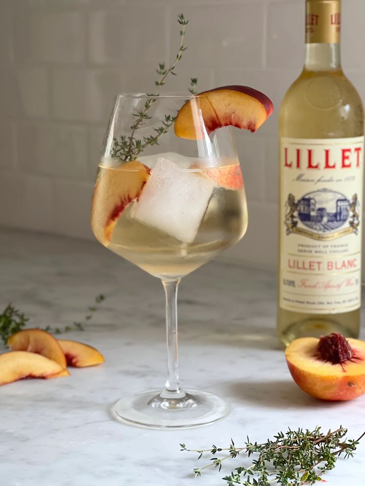 a glass filled with liquid next to a bottle and sliced peaches on a table