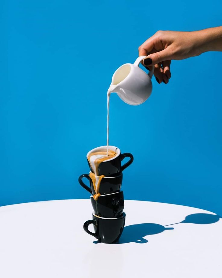 a person pours coffee into two black mugs on a white table against a blue background