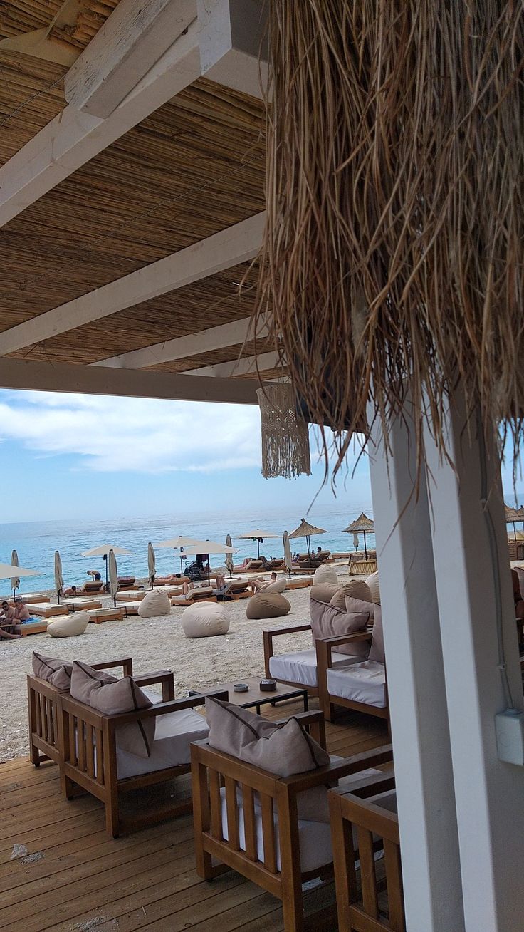 chairs and umbrellas are set up on the deck overlooking the beach in front of an overhang