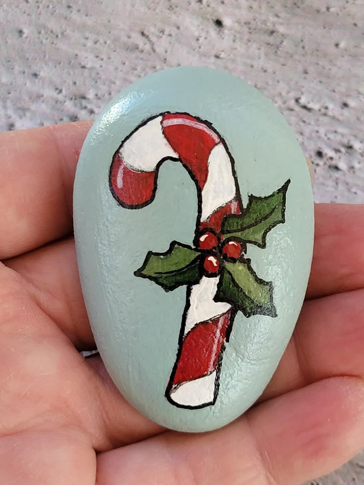 a hand holding a rock with a candy cane painted on it's side,