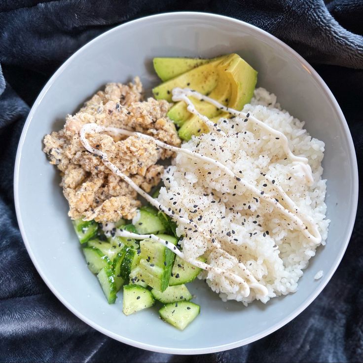 a white bowl filled with rice, cucumber and other food items on top of a blue blanket