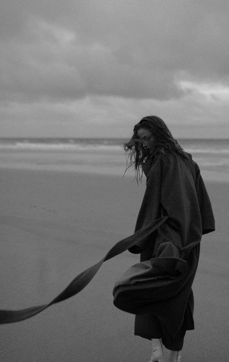 a woman walking on the beach with her long hair blowing in the wind