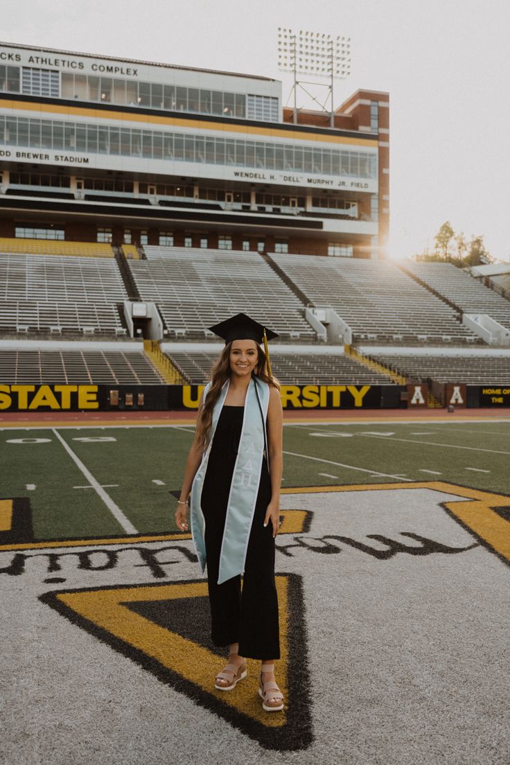 a woman in graduation cap and gown standing on the football field