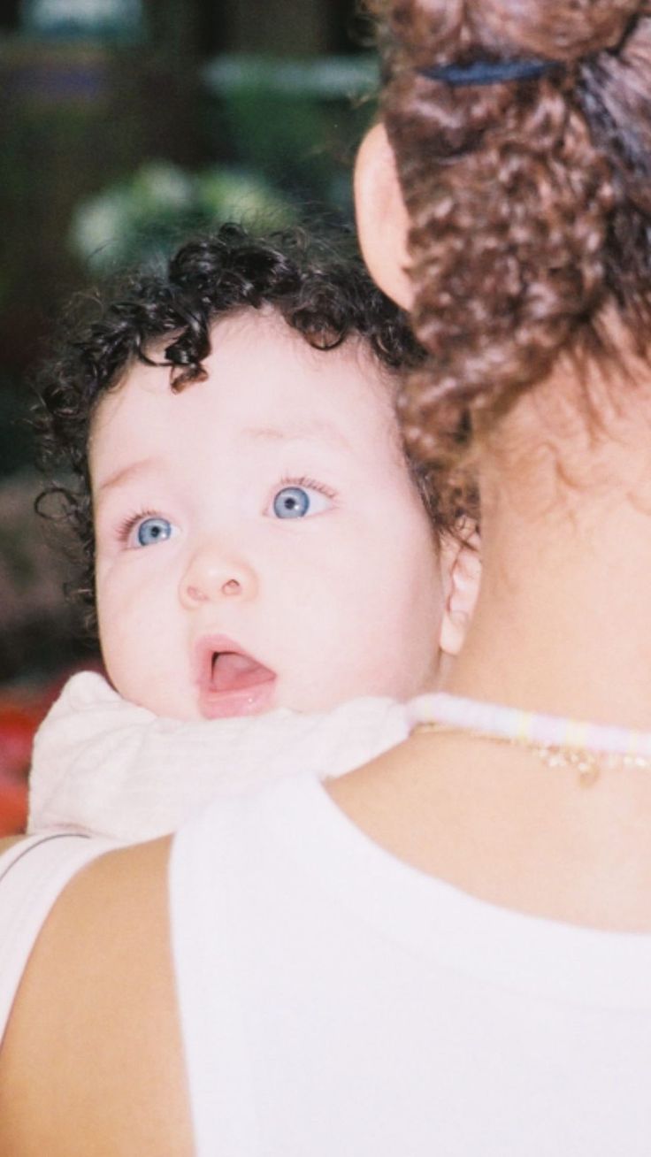 a woman holding a baby in her arms and looking at the camera with blue eyes