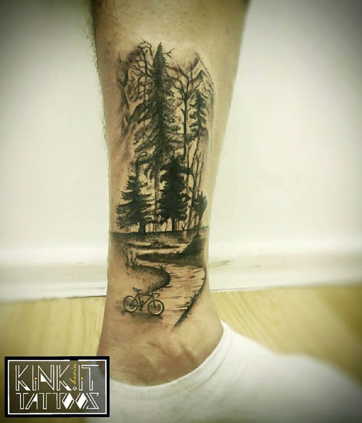 a man's leg with a tattoo on it that has trees and a bike in the water