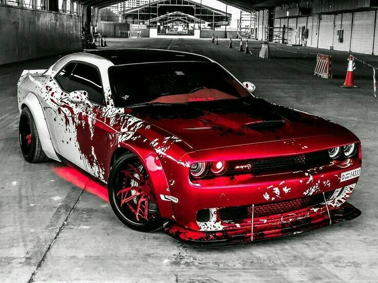 a red and white car parked in a parking garage with graffiti on it's hood