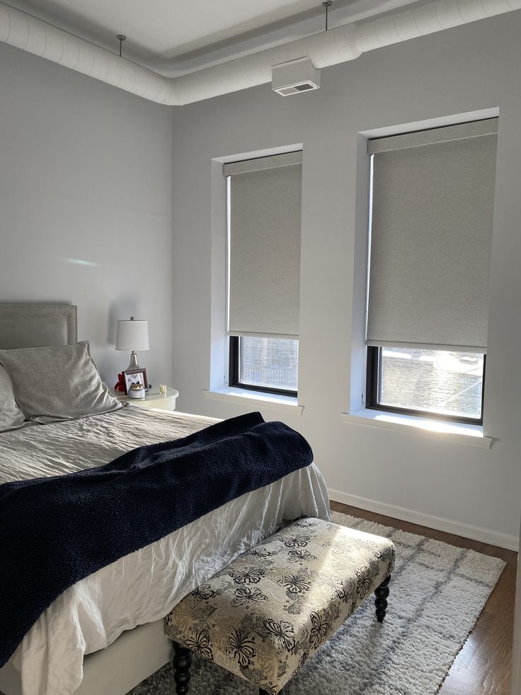 a bedroom with two windows and a bench in front of the bed, along with a rug on the floor