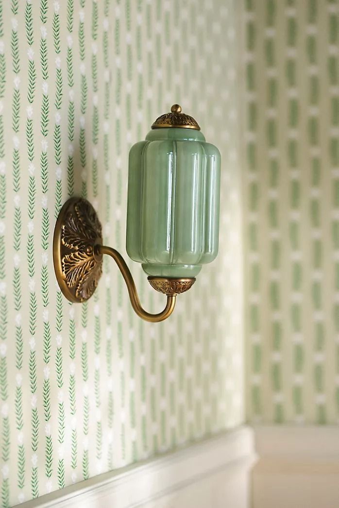 a green glass light fixture on the wall in a room with white walls and patterned wallpaper