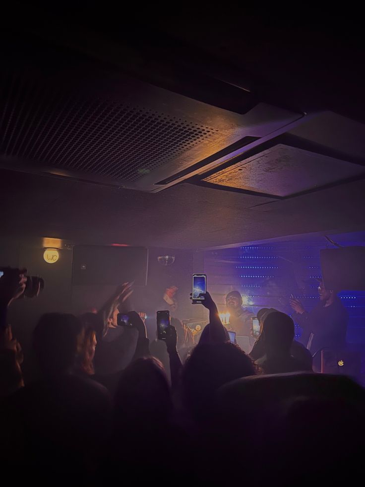 a group of people standing in front of a crowd holding up cell phones to take pictures