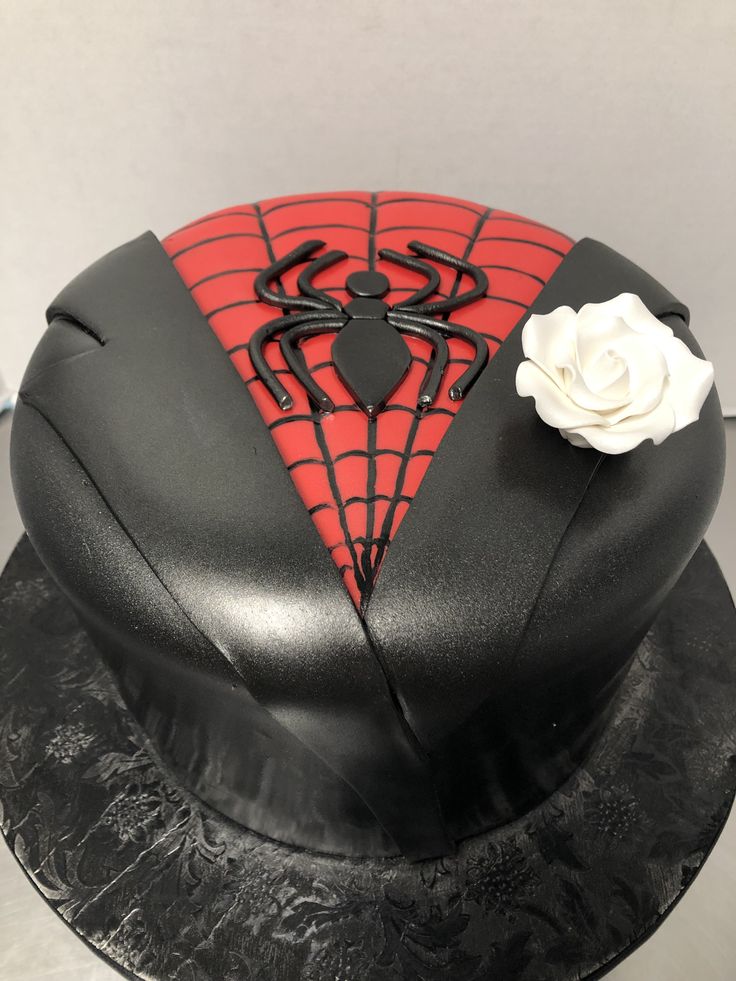 a spiderman cake is decorated with black icing and red fondant, topped with a white rose