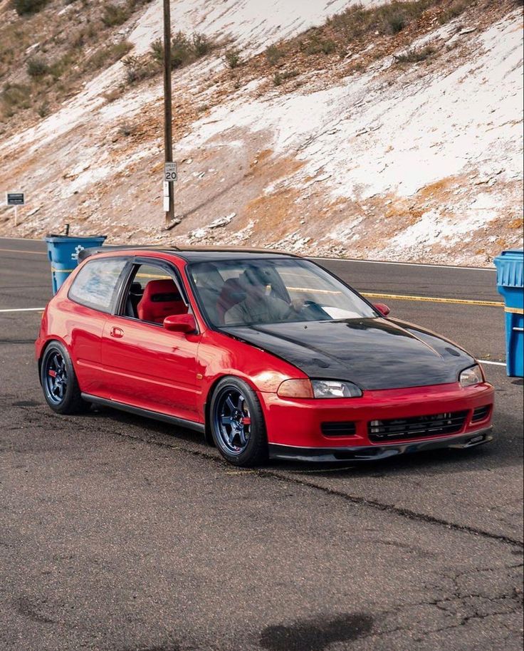 a red car parked on the side of a road next to a blue trash can