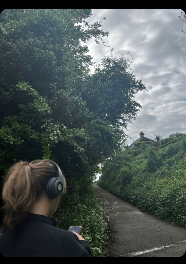 a woman with headphones is looking at the sky over a path that leads to a small house