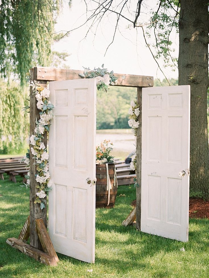 two white doors with flowers on them are in the grass near a tree and bench