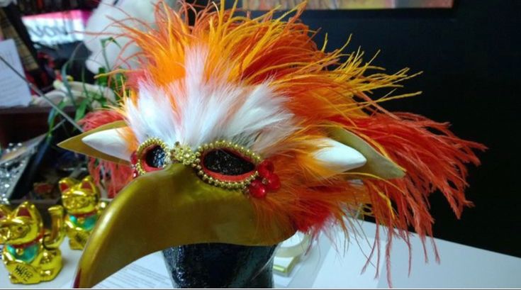 an orange and white feathered mask on display in a vase with other decorations behind it