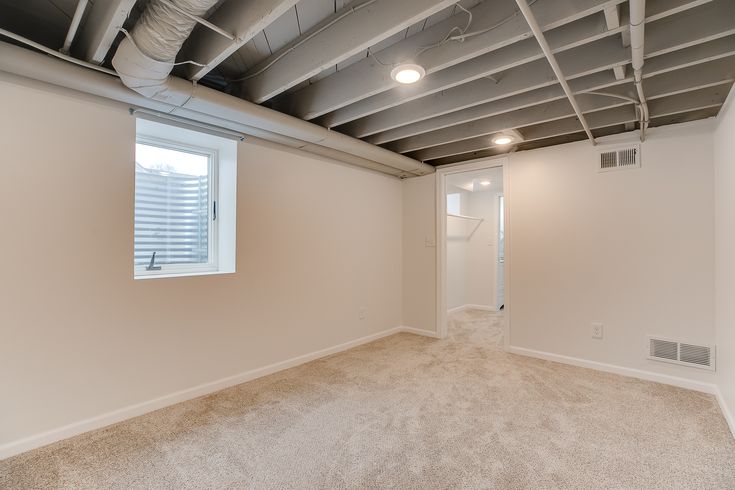 an empty room with white walls and exposed ceiling beams, carpeted flooring and a large window