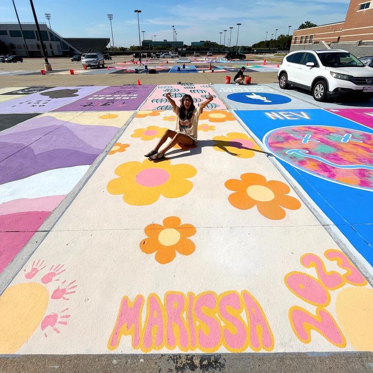 a woman sitting on the ground in front of a parking lot with flowers painted on it