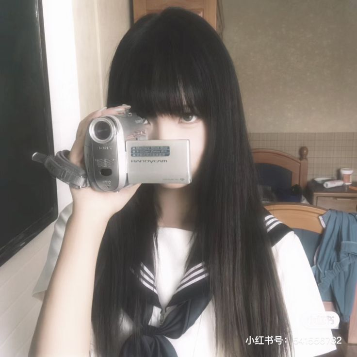 a girl with long black hair holding up a camera