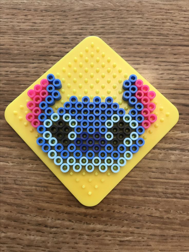 a yellow square with blue and red beads on it sitting on top of a wooden table