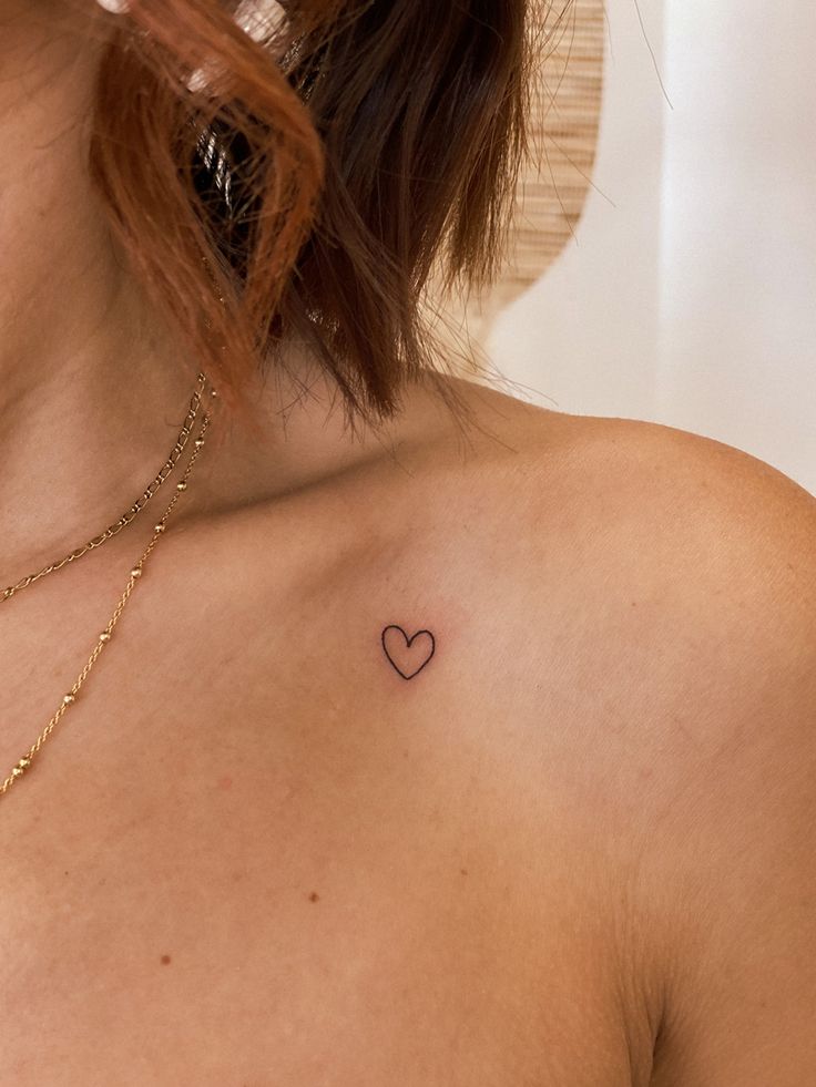 a woman's chest with a small heart tattoo on the left side of her chest